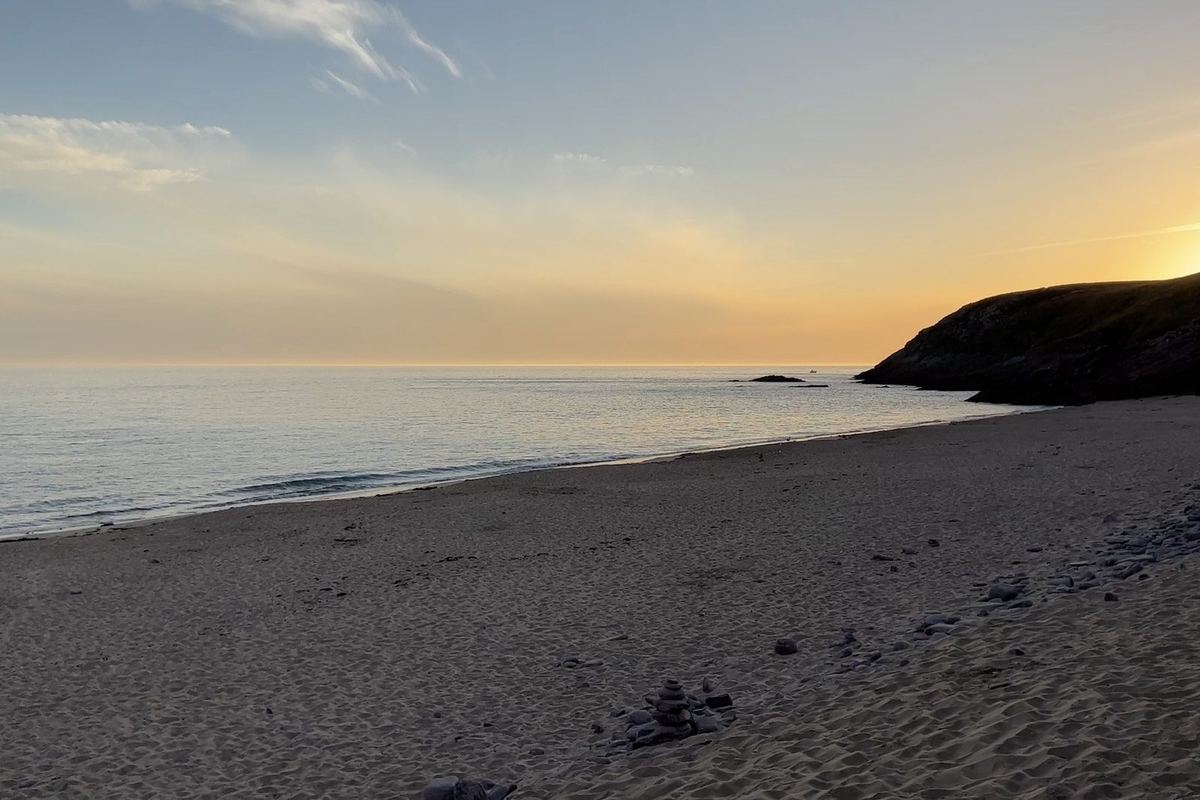 Coucher de soleil sur une plage du secteur : mer étale, sable strié et ciel orangé au-dessus de la pointe